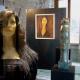 Manichino che si fa fotografare davanti a delle opere di una mostra di Modigliani