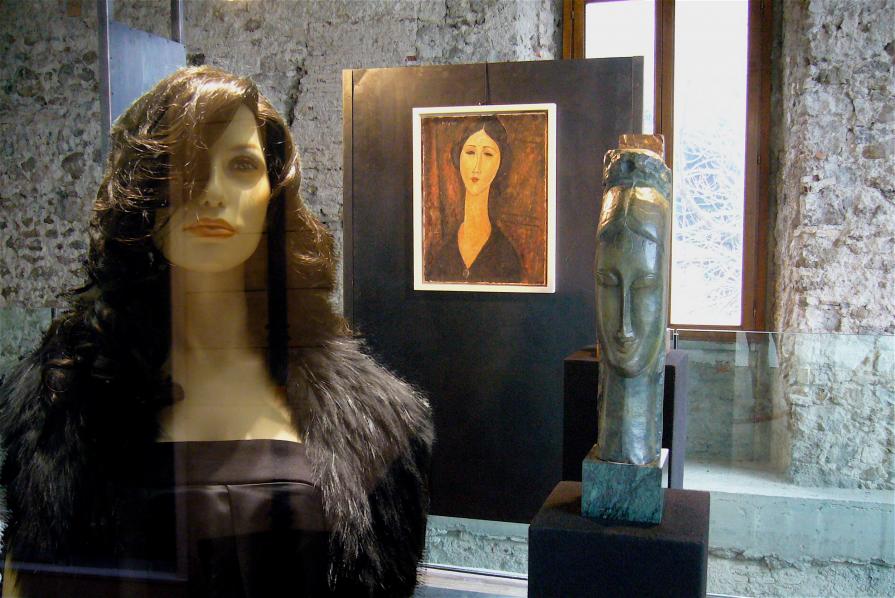 Manichino che si fa fotografare davanti a delle opere di una mostra di Modigliani